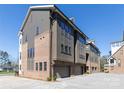 Rear view of three-story townhomes featuring brick, gray siding, and individual two-car garages at 3115 Pinehurst Pl, Charlotte, NC 28209