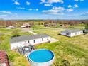 Aerial view of a home with an above ground pool set in a lush green backyard surrounded by trees and open fields at 590 County Line Rd, Stony Point, NC 28678
