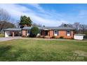 Charming single-story red brick home with a covered carport, a well-manicured lawn, and mature trees at 2704 Silvers Ln, Albemarle, NC 28001