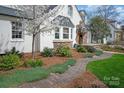 Landscaped front yard featuring a winding brick path, mature trees, and a freshly painted white brick facade at 2237 Colony Rd, Charlotte, NC 28209