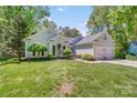 Inviting home featuring a lush green lawn, mature trees, and a convenient two-car garage at 11003 Pale Hickory Ln, Charlotte, NC 28215