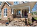 Inviting covered front porch featuring stone accents, rocking chairs, and an elegant entrance door at 7806 Spanish Oaks Dr, Waxhaw, NC 28173