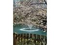 Scenic pond view featuring a water fountain framed by blooming cherry trees and a rustic wooden fence at 20313 Queensdale Dr, Cornelius, NC 28031