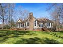 Rear exterior featuring a stone chimney, multiple windows, and a backyard with mature trees at 147 Pearl Bay Dr, New London, NC 28127