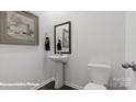 A well-lit half bathroom featuring modern pedestal sink, toilet, and decorative mirror at 8051 Plymouth Dr, Sherrills Ford, NC 28673