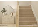 View of a staircase with tan carpeting complemented by a modern table and mirror at 1816 Otter Perch Ln, Fort Mill, SC 29715