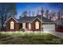 Charming one-story brick home with well-manicured lawn, American flag, and attached two-car garage at dusk at 801 Toncin Ave, Bessemer City, NC 28016