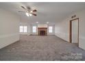 Spacious living room with a cozy brick fireplace, neutral carpet, ceiling fan, and large windows for natural light at 40701 Nc 740 Hwy, New London, NC 28127