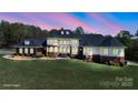 A stunning exterior shot of a large home with a manicured lawn, brick accents, and many windows glowing in the evening light at 447 Willow Pond Ln, Hiddenite, NC 28636