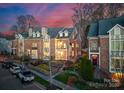 Charming brick townhome showcases a well-manicured lawn, flowering shrubbery, and multiple decks beneath a dramatic sunset sky at 415 Spring St, Davidson, NC 28036