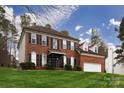 A shot of an elegant two-story brick house featuring dark shutters and a lush, green lawn under a bright sky at 10928 Jardin Way, Charlotte, NC 28215