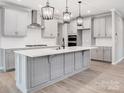 Bright kitchen features an island with pendant lighting, stainless hood, light wood floors and light gray cabinetry at 9934 Cask Way, Huntersville, NC 28078