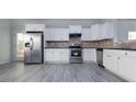 Modern kitchen featuring stainless steel appliances, granite countertops, white cabinets, and gray wood floors at 3308 Lemongrass Ln, Charlotte, NC 28214