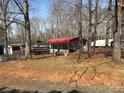 Exterior shot of the home featuring a red awning, boats, and gravel parking surrounded by mature trees at 149 Deer Park Rd # D26/27, Mount Gilead, NC 27306