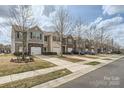A row of townhomes featuring neutral siding, stone accents, attached garages, driveways, and street view at 9035 Bradstreet Commons Way, Charlotte, NC 28215