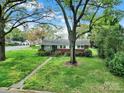 Quaint single-story home with brick and white accent, surrounded by a large yard and mature trees for privacy at 5876 Wedgewood Dr, Charlotte, NC 28210