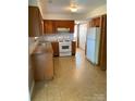 Functional kitchen with oak cabinets, white appliances, and neutral tile flooring at 7307 Meadowland Dr, Charlotte, NC 28215