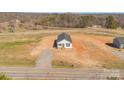Expansive aerial view of a quaint white home with a dark roof, surrounded by undeveloped land and clear blue skies at 603 Mt. Wesley Church Rd, Hiddenite, NC 28636