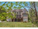 Rear view of a brick home with a covered porch and balcony, surrounded by lush greenery and blue skies at 4300 Old Course Dr, Charlotte, NC 28277