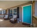 Inviting front porch with wicker chairs, a vibrant teal door, and charming decorative details at 7790 Caswell Rd, Stanley, NC 28164