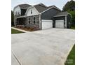 View of the home's side with a spacious concrete driveway, a two-car garage, and stone and gray siding at 7001 New Town Rd, Waxhaw, NC 28173