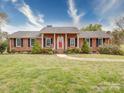 Inviting brick house featuring a symmetrical facade, red door, and manicured landscaping, enhanced by a stone walkway at 24436 Nc 24/27 Hwy, Albemarle, NC 28001