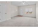 Bright living room featuring neutral walls, plush carpeting, ceiling fan, and a front door with transom window at 12550 Mcgrath Dr, Charlotte, NC 28269