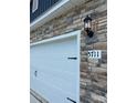 A two car garage featuring stone accents and a carriage door with an address marker at 5711 Skinny Dr, Charlotte, NC 28215