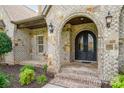 Close up of arched brick entryway with a wrought iron front door, beautiful stonework, and elegant outdoor lighting at 4904 Ardenetti Ct, Mint Hill, NC 28227