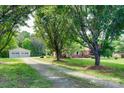 Quaint brick home with mature trees and a detached garage, accessible by a gravel driveway and lush green lawn at 904 Sunbeam Dr, Lincolnton, NC 28092