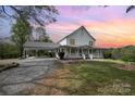 Charming two-story home with a long porch and a spacious carport, set against a beautiful sunset sky at 1151 Trull Hinson Rd, Wingate, NC 28174