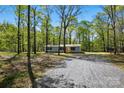 Single-story home featuring gray siding, black shutters and a gravel driveway through the trees at 110 Matthew Dr, Kings Mountain, NC 28086