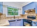 Kitchen featuring blue cabinets, stainless steel sink, and modern appliances illuminated by a bright window at 1409 Sherwood Dr, Kannapolis, NC 28081