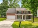Traditional brick home with a covered front porch, surrounded by lush greenery and mature trees at 1014 Sandbox Cir, Indian Trail, NC 28079