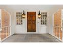 Covered front porch featuring a paneled wood door, decorative sconces, and gray tile flooring at 1441 Carmel Rd, Charlotte, NC 28226