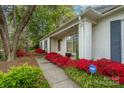 The beautiful home has a white brick exterior with a walkway bordered with vibrant azaleas leading to the front door at 6815 Old Post Rd, Charlotte, NC 28212