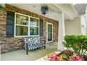 Inviting front porch with stone accents, bench seating, decorative plants, and a hanging flower basket at 13715 Sunrise View Dr, Charlotte, NC 28278