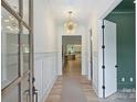 Inviting hallway with hardwood floors, white wainscoting, a statement light fixture, and a partial view of the kitchen at 5010 Ohm Ln, Charlotte, NC 28270