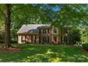 Classic brick home featuring a manicured lawn and mature trees creating a serene and private setting at 6017 Summerston Pl, Charlotte, NC 28277