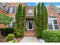 Inviting front entrance with a glass door, brick steps, and manicured landscaping, enhanced by tall evergreens at 7302 Yellowhorn Trl, Waxhaw, NC 28173