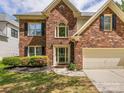 Two-story brick home with attached two-car garage, blooming shrubs, and mature trees in a landscaped yard at 7409 Tarland Ln, Charlotte, NC 28269