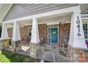 Inviting front porch with stone pillars, brick accents, and a teal front door with stylish decor at 10416 Glenmac Rd, Charlotte, NC 28215