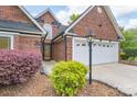 Close up view of the brick home showcasing landscaping, front door, and two-car garage at 2104 Planters Knoll Dr, Monroe, NC 28110