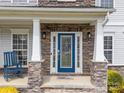 Inviting front porch with a blue door and stone pillars at 8453 Mossy Cup Trl, Harrisburg, NC 28075