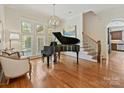 Elegant living room with a grand piano, large windows, hardwood floors, and staircase access at 7208 Ashton Gate Dr, Charlotte, NC 28270