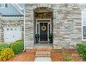 Charming stone home featuring a black front door with decorative wreath and manicured landscaping at 1005 Argentium Way, Waxhaw, NC 28173