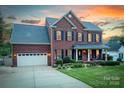 Charming two-story brick home featuring a well-manicured lawn and inviting front porch at sunset at 220 Chandeleur Dr, Mooresville, NC 28117