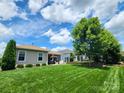 A well-maintained backyard featuring a green lawn, patio with outdoor furniture, and lush landscaping under a bright, partly cloudy sky at 4831 Looking Glass Trl, Denver, NC 28037