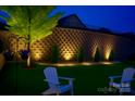 A landscaped backyard with strategic lighting highlighting a retaining wall, trees, and patio area with two Adirondack chairs at 4831 Looking Glass Trl, Denver, NC 28037