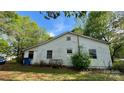 Rear view of a cozy home with white siding, windows, propane tank, and a large lawn, surrounded by mature trees at 2118 Polkville Rd, Shelby, NC 28150